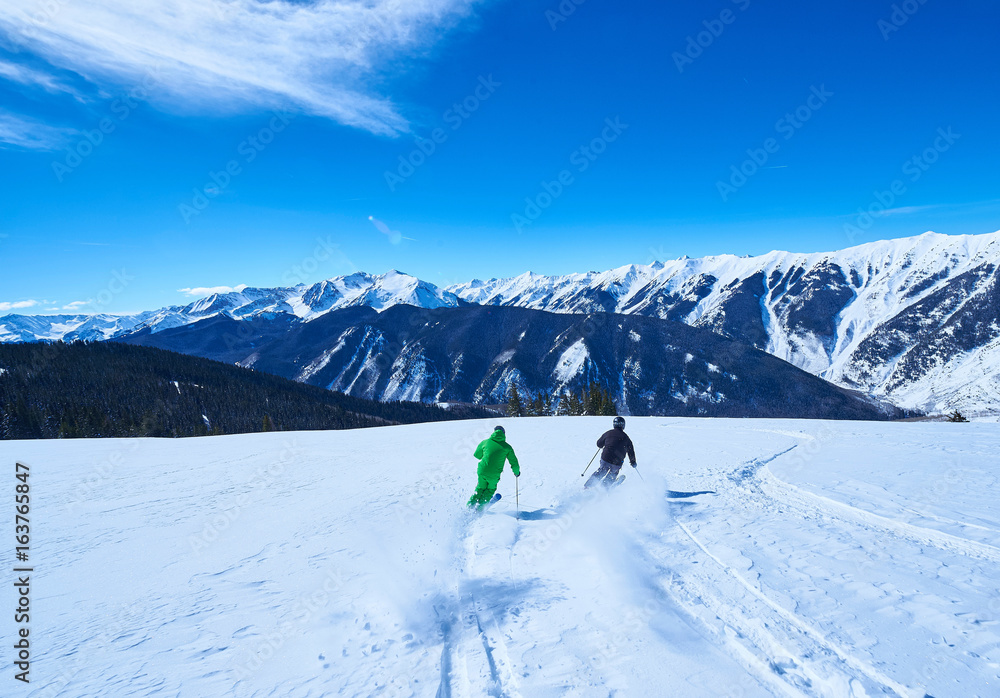 Rear view of two men skiing down snow covered ski slope, Aspen, Colorado, USA Rear view of two men skiing down snow covered ski slope, Aspen, Colorado, USA
