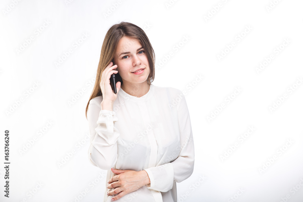 Beautiful young girl in a white shirt on white isolated background talking on a mobile phone. Smiles portrait to the waist Beautiful young girl in a white shirt on white isolated background talking on a mobile phone. Smiles portrait to the waist