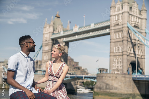 Young couple sitting on wall, smiling, Tower Bridge in background, London, England, UK photo