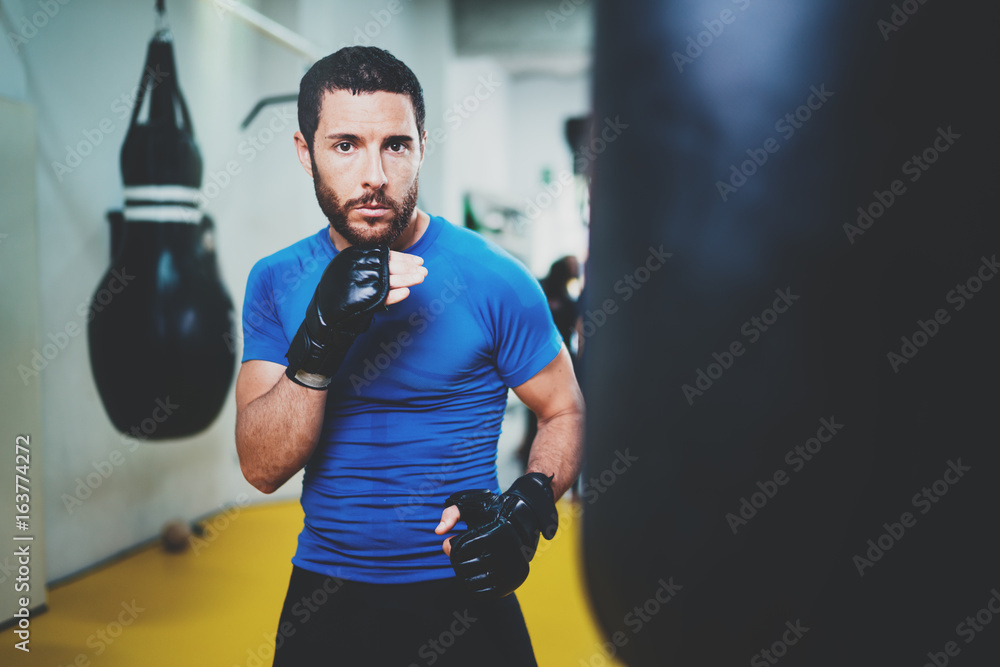 Concept of a healthy lifestyle.Young athlete fighter practicing kicks with punching bag.Kick boxer boxing as exercise for the fight.Boxer man hits punching bag.Horizontal.
