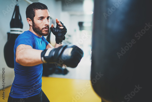 Concept of a healthy lifestyle.Young muscular man fighter practicing kicks with punching bag.Kick boxer boxing as exercise for the fight.Boxer hits punching bag.Horizontal. © SFIO CRACHO