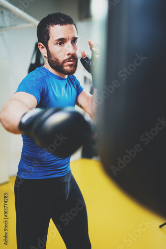 Concept of a healthy lifestyle.Young athlete fighter practicing kicks with punching bag.Kick boxer boxing as exercise for the fight.Boxer man hits punching bag.Vertical. © SFIO CRACHO