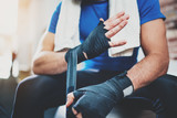 Muscular Boxer man prepairing hands for hard kickboxing training session in gym. Young athlete tying black boxing bandages.Blurred background. Horizontal.