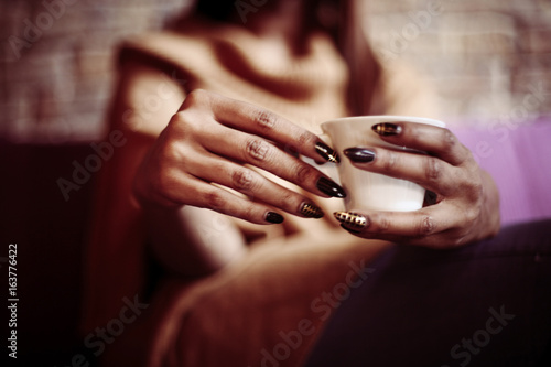 Hands of African American woman holding a coffee mug. Close up, woman hands holding cup of coffee.