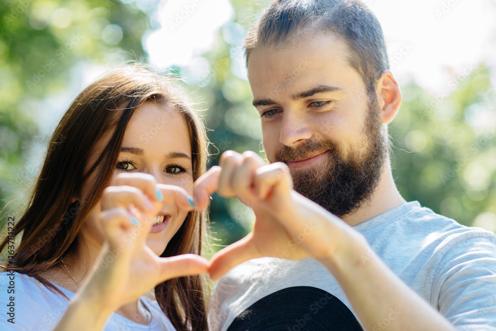 Closeup shot of young hansome beard man and smiling woman making heart shape with hand. Loving couple making heart shape with hands outdoor. Female and male hands making up heart shape. Closeup shot of young hansome beard man and smiling woman making heart shape with hand. Loving couple making heart shape with hands outdoor. Female and male hands making up heart shape.