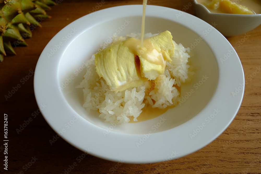 Pouring coconut milk on the sticky rice toping with durian on the wooden table