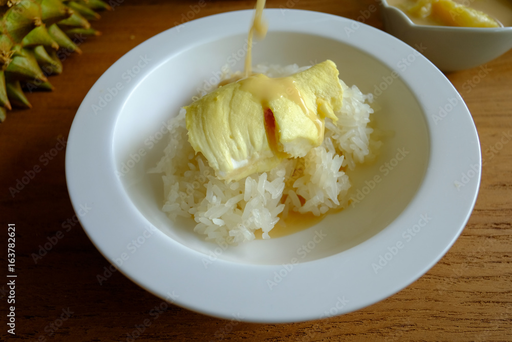 Pouring coconut milk on the sticky rice toping with durian on the wooden table