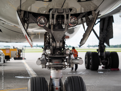 Chassis and headlights of a large white aircraft. Behind the chassis is seen an employee of the maintenance staff in an orange j