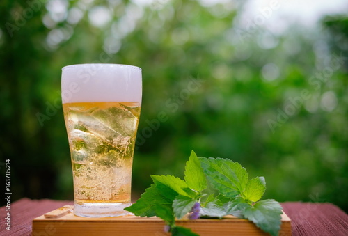 Golden beer in glass with green leaf on wooden box with blur green nature background. Prevent heart disease and help reduce high blood pressure. photo