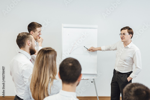 Business meeting at office. Handsome man presenting charts on whiteboard to team. Multi ethnic group of people