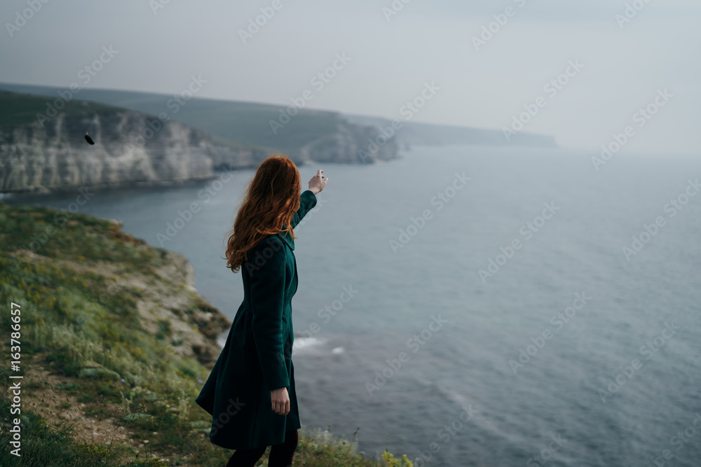 Beautiful young woman standing on a cliff near the sea