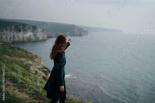 Beautiful young woman standing on a cliff near the sea