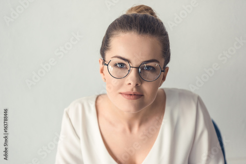 attractive stylish businesswoman in eyeglasses sitting in modern office