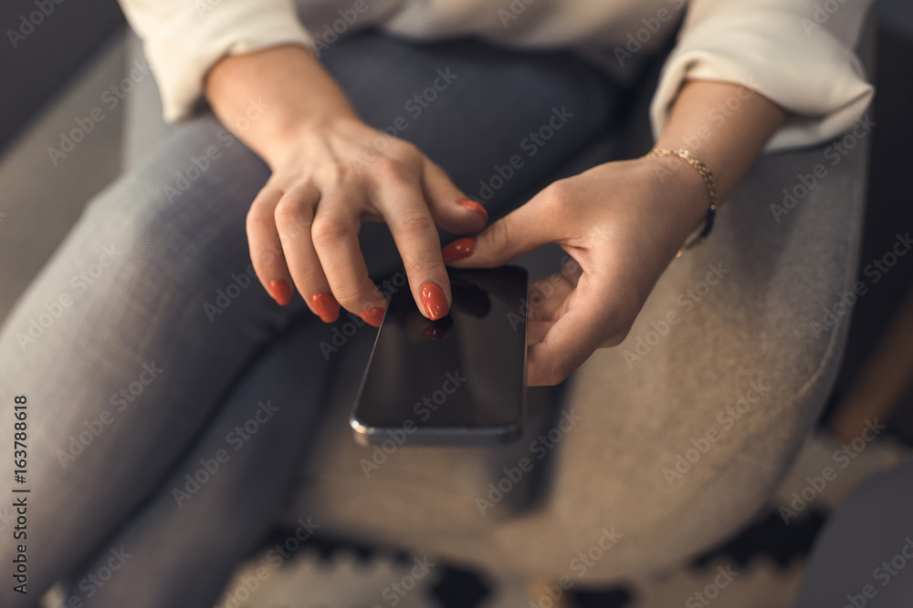 cropped view of female hands with red manicure using smartphone