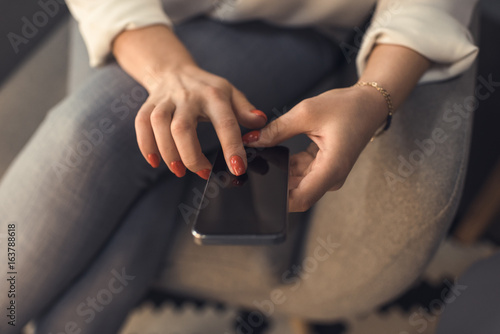 cropped view of female hands with red manicure using smartphone