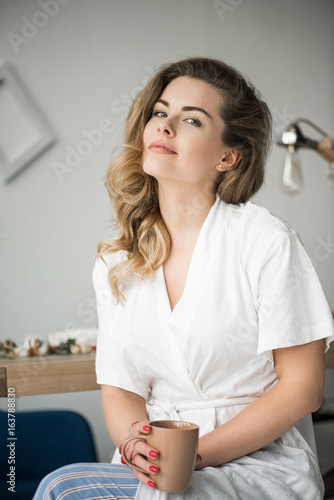 portrait of attractive blonde woman in white robe holding coffee cup