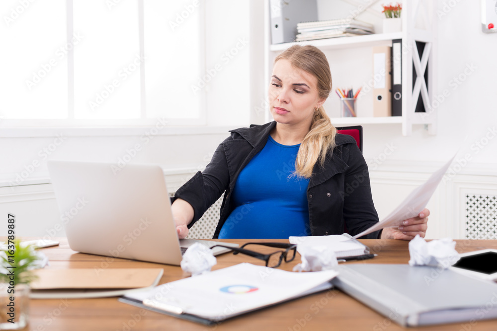 Pregnant business lady at work reading papers Pregnant business lady at work reading papers