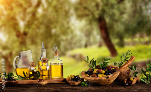 Freshly harvested olives berries in wood bowls and pressed oil in glass bottles