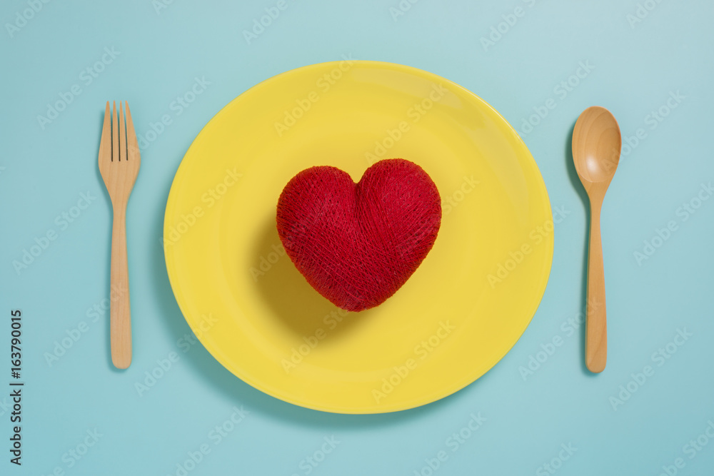 Flat lay of red heart on yellow plate with fork on pastel blue color background Flat lay of red heart on yellow plate with fork on pastel blue color background