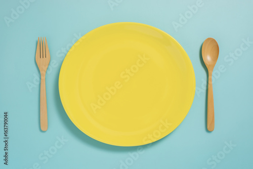 Flat lay of tableware, yellow plate and fork on pastel blue color background