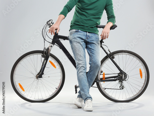 Handsome young man with bicycle on light background