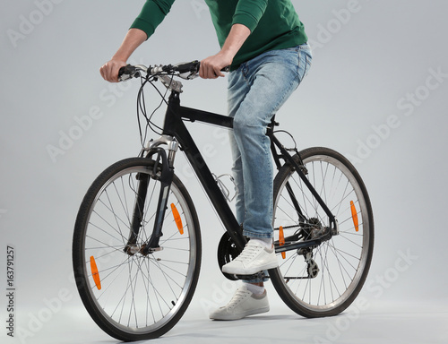 Handsome young man with bicycle on light background