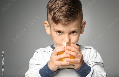 Cute little boy drinking juice on grey background, closeup