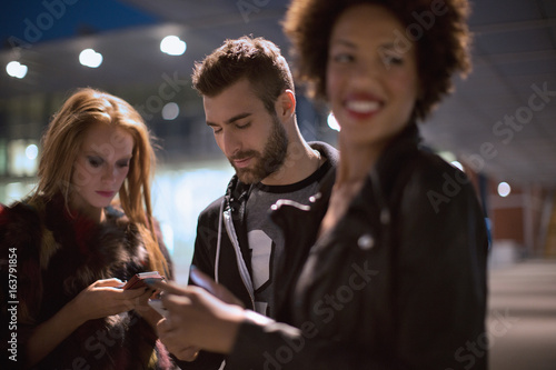 Friends going out checking mobile phones at train station at night photo