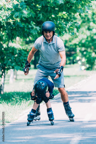 Grandfather and grandson having fun, roller skating in the park