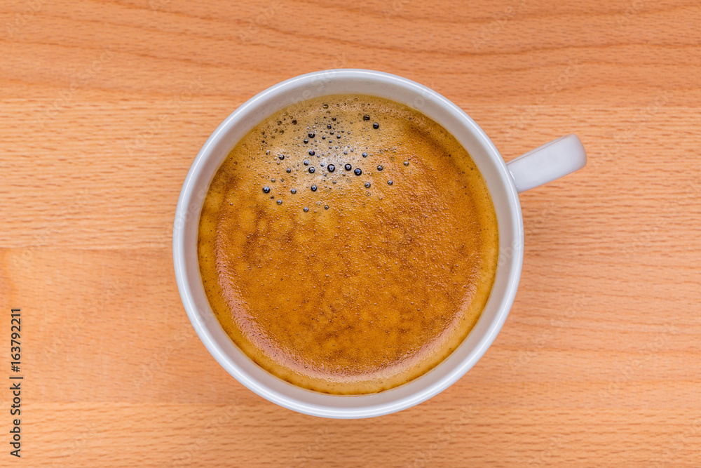 Hot black coffee with foam bubbles in white cup with wooden board in background, morning coffee concept. Hot black coffee with foam bubbles in white cup with wooden board in background, morning coffee concept.