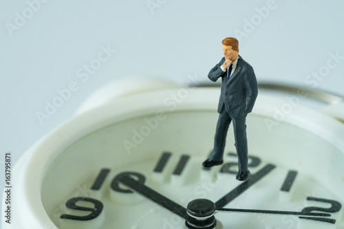 business or time countdown concept with miniature businessman thinking figure standing on white alarm clock
