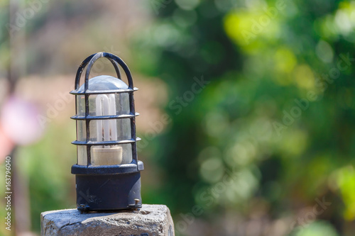 Light bulb on concrete pole with green bokeh background.