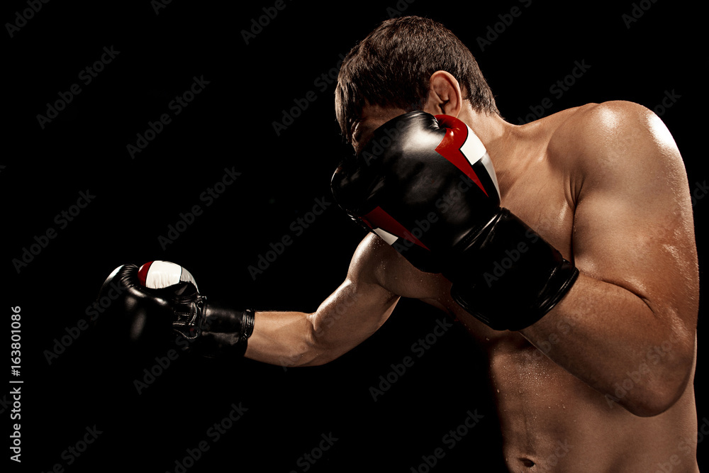 Male boxer boxing in punching bag with dramatic edgy lighting in a dark studio Male boxer boxing in punching bag with dramatic edgy lighting in a dark studio