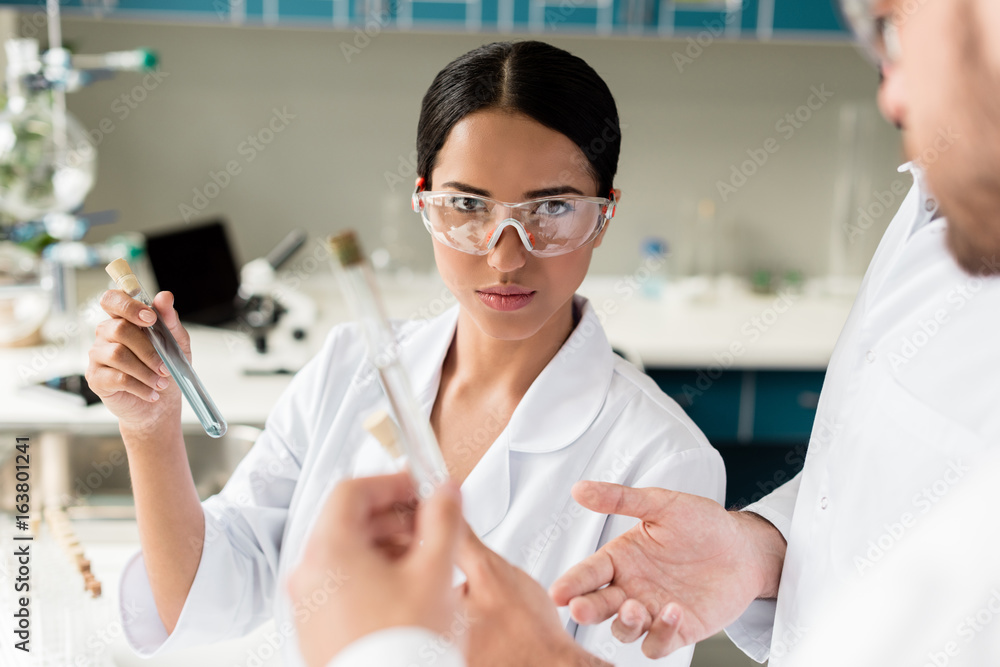 Young female scientist holding test tube with reagent and looking at camera in lab Young female scientist holding test tube with reagent and looking at camera in lab