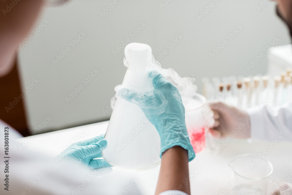 Fototapeta premium Close-up partial view of scientists making experiment with reagent and flasks