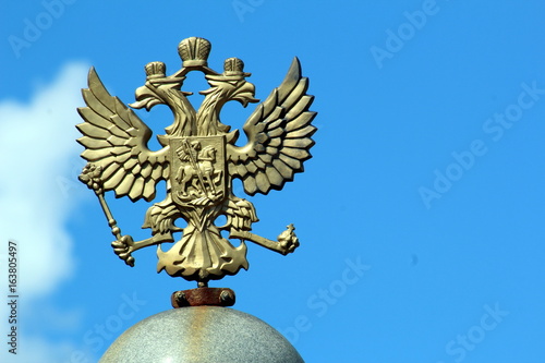 Coat of arms of Russia in bronze in the form of a two-headed eagle against the blue sky.