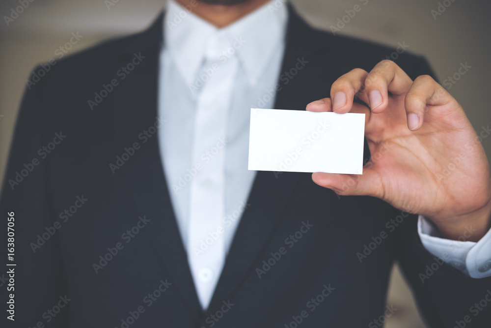 A business man in white shirt and gray suit holding and showing empty business card A business man in white shirt and gray suit holding and showing empty business card