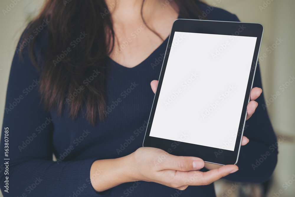 Mockup image of a business woman holding and showing black tablet with blank white screen in office
