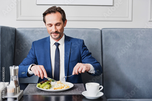 Joyful businessman eating dish in cafe