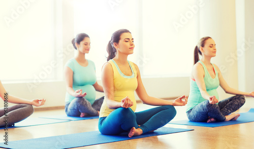 happy pregnant women exercising yoga in gym