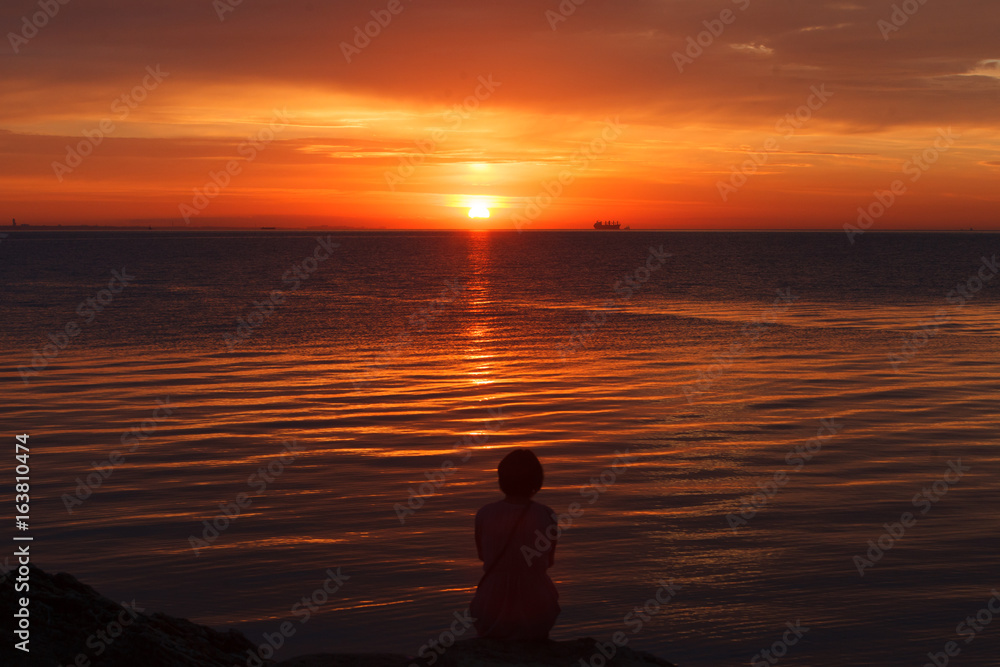 Lonely girl sitting on the beach and meets the dawn