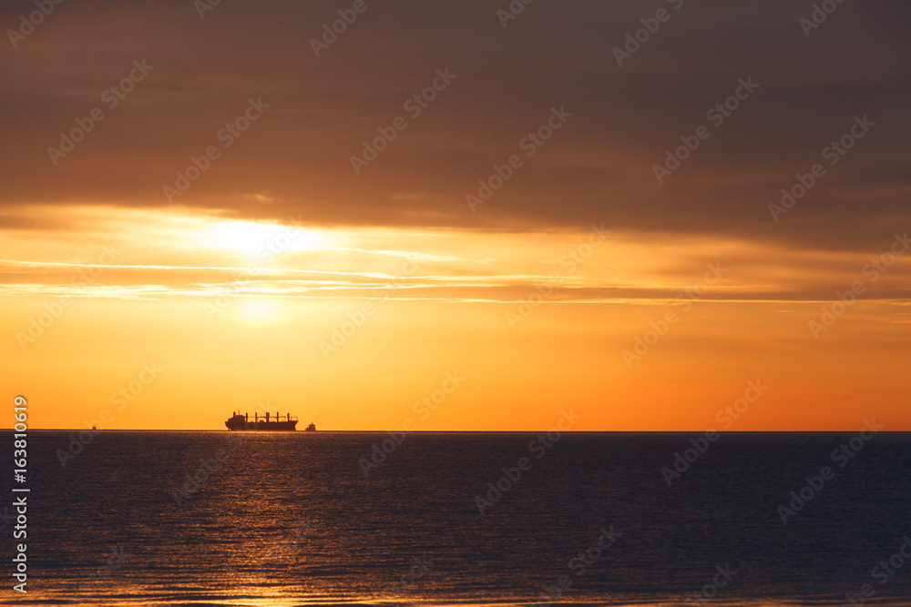 Dawn at the sea. In the distance a ship can be seen.