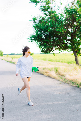 Beautiful young girl running with a skateboard in hands. Smiling