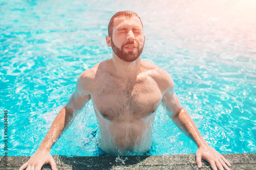 Summer photo of muscular smiling man in swimming pool. Happy male model in water on summer vacations.
