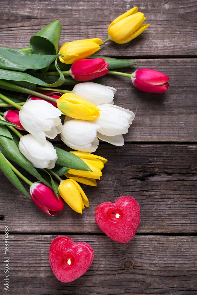 Two red burning candles in form of heart and bright tulips flowers Two red burning candles in form of heart and bright tulips flowers