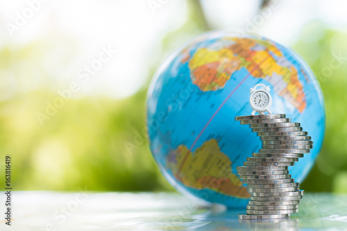 A globe with a map of the world behind a white clock on the stack of coins. money, financial and business growth concept.