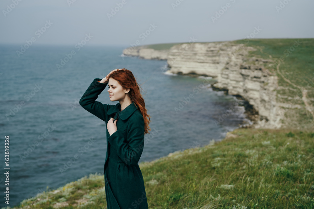 Beautiful young woman standing on a cliff near the sea