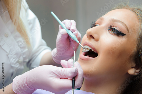 Doctor in uniform checking up female patient's teeth in dental clinic