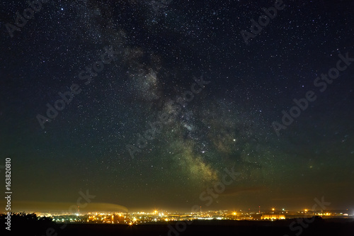 Starry night sky with the Milky Way over the city with lighting.