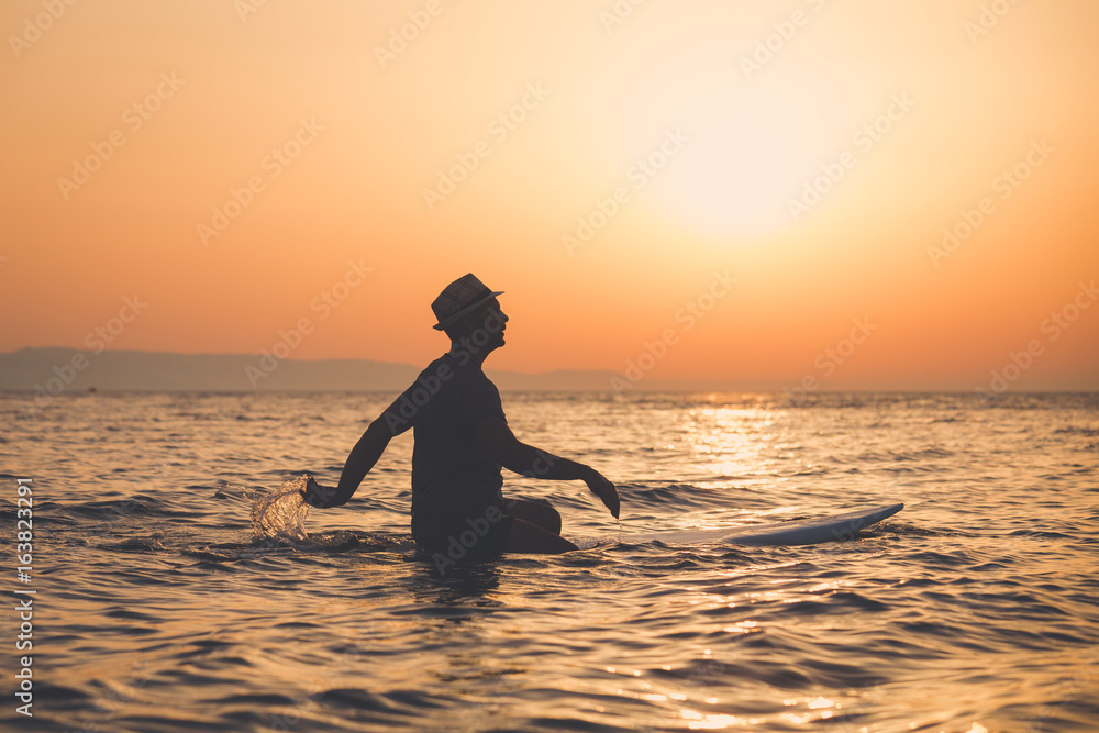 Silhouette of man sitting on surfboard at sunset over sea